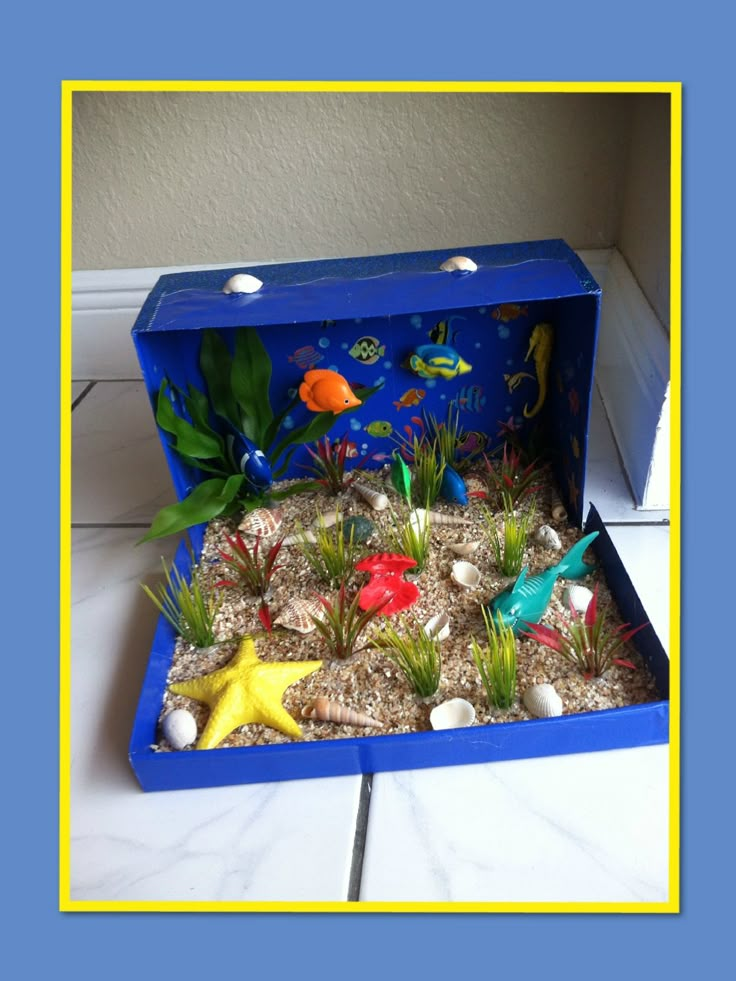 an open blue box filled with small plants and sea animals on top of a white tile floor