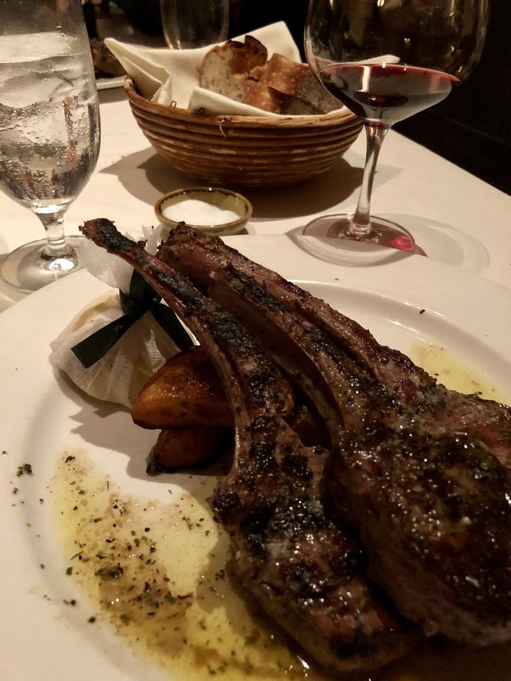 a plate with steak and potatoes on it next to wine glasses, bread and water