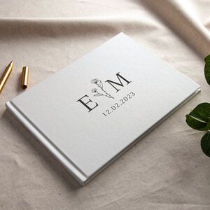 a wedding guest book and pen sitting on a table next to some green leaves with the initials e m