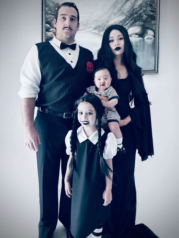 a family dressed up for halloween standing in front of a wall with a painting on it