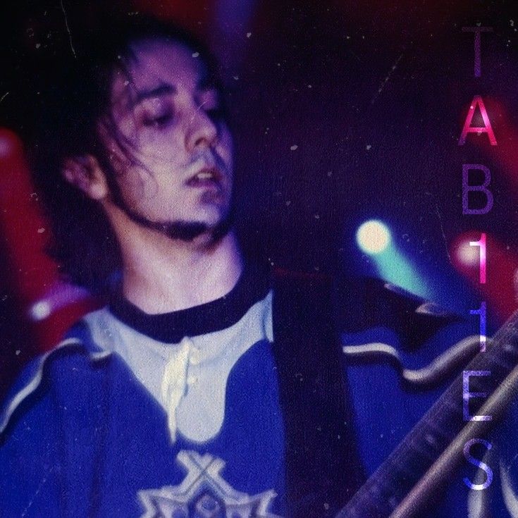 a man holding a guitar in his right hand and wearing a blue shirt with white letters on it