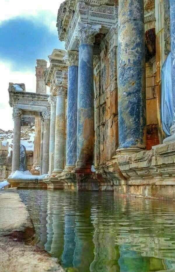 an old building with columns and water in the foreground