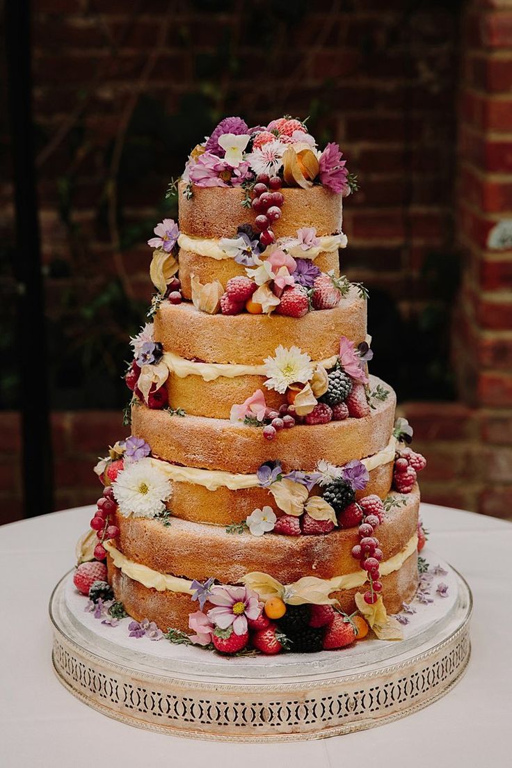 a multi layer cake with flowers on top is sitting on a table in front of a brick wall