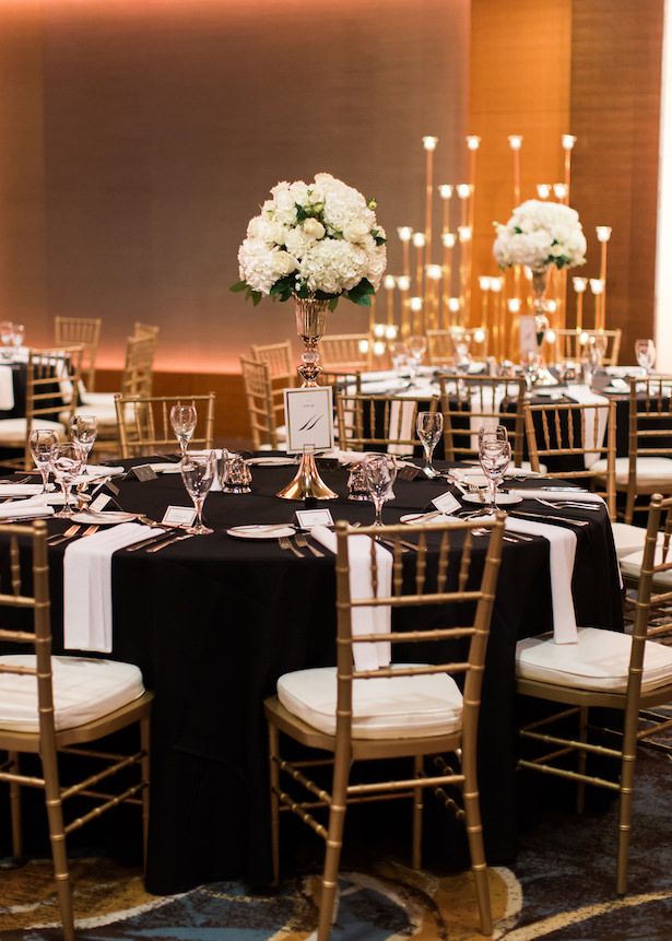 the tables are set with black and white linens, gold chairs, and centerpieces