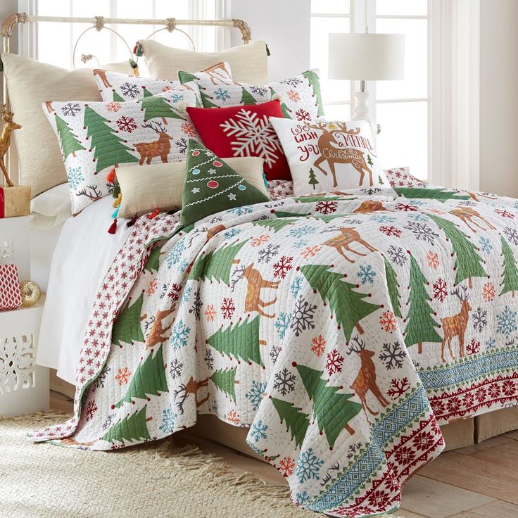 a bed covered in christmas themed comforters and pillows with deers on them, sitting next to a window