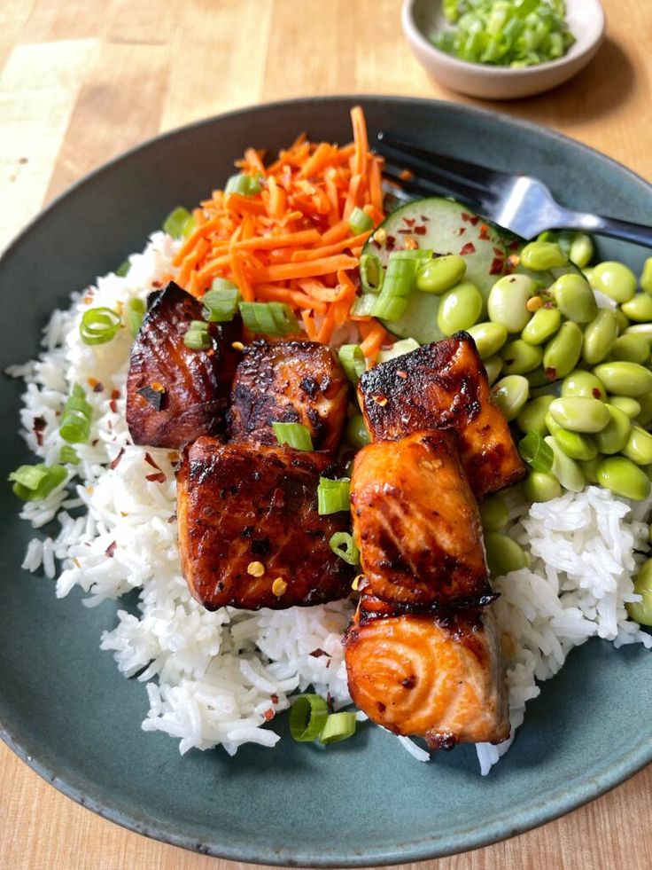 a blue plate topped with meat, rice and veggies on top of a wooden table