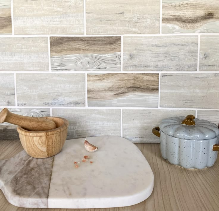 a wooden bowl sitting on top of a cutting board next to a wall with white tiles