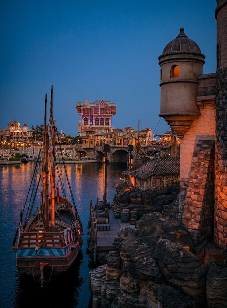 a boat that is sitting in the water next to some buildings and a bridge at night