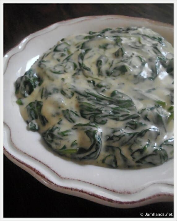 a white plate topped with spinach covered in cheese and sauce on top of a wooden table