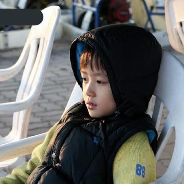 a young boy sitting on top of a white chair next to another child wearing a black jacket