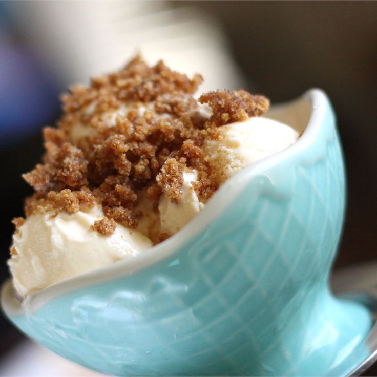 an ice cream sundae with crumbled toppings in a blue ceramic bowl