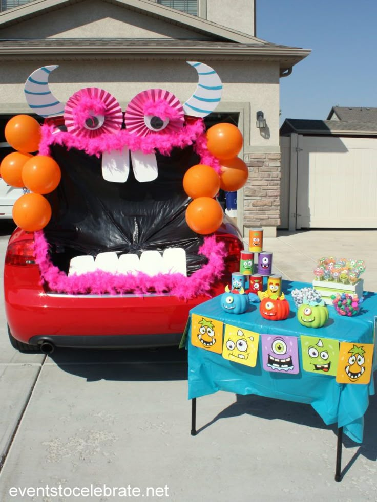 a car decorated with decorations and balloons in the shape of monster heads is parked next to a party table