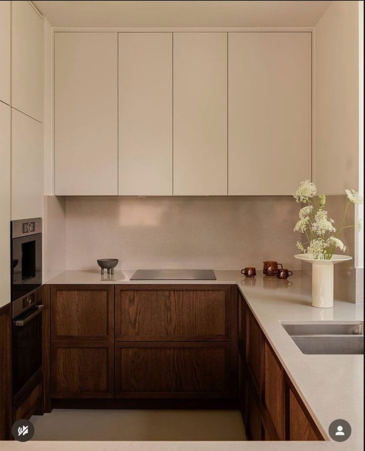 a white kitchen with wooden cabinets and a vase filled with flowers on the counter top