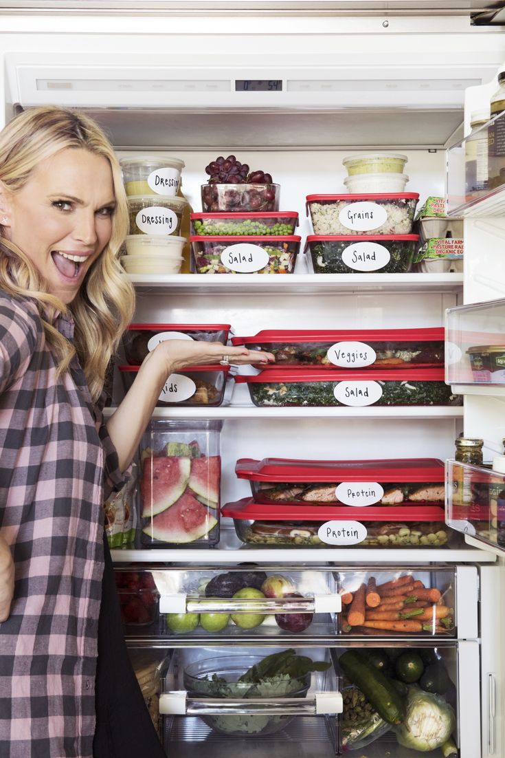 a woman standing in front of an open refrigerator filled with food and vegetables, smiling at the camera