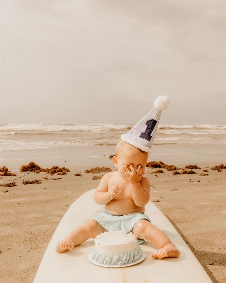 a baby sitting on top of a surfboard wearing a birthday hat