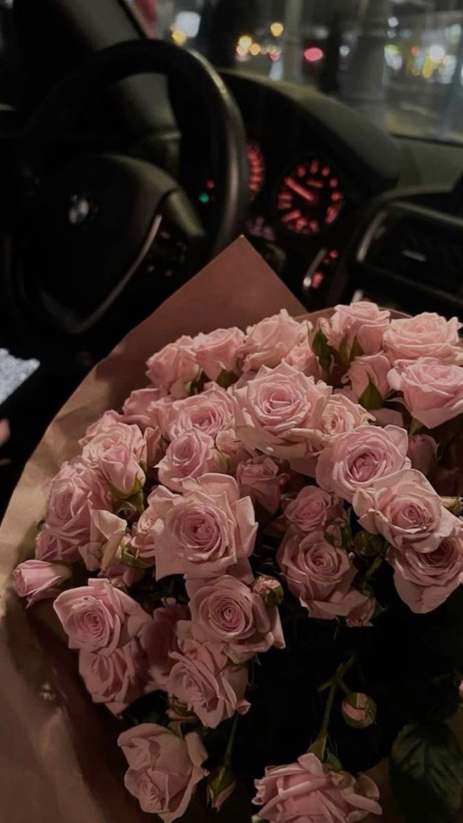 a bouquet of pink roses sitting on top of a table next to a steering wheel