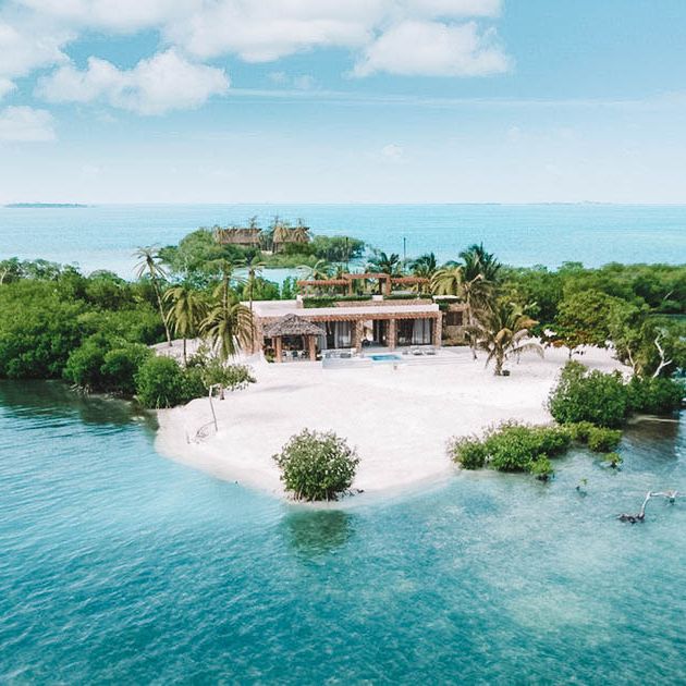 an island in the middle of some water with houses on it and palm trees around