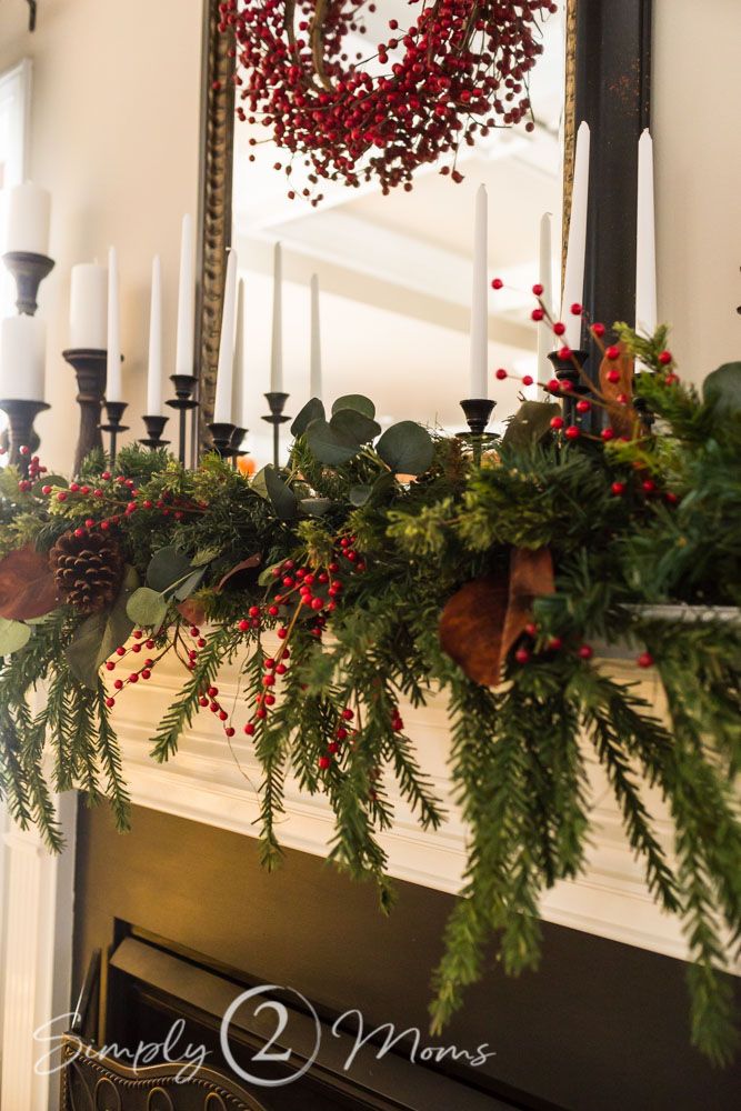 a fireplace mantel decorated for christmas with greenery, berries and candles on it