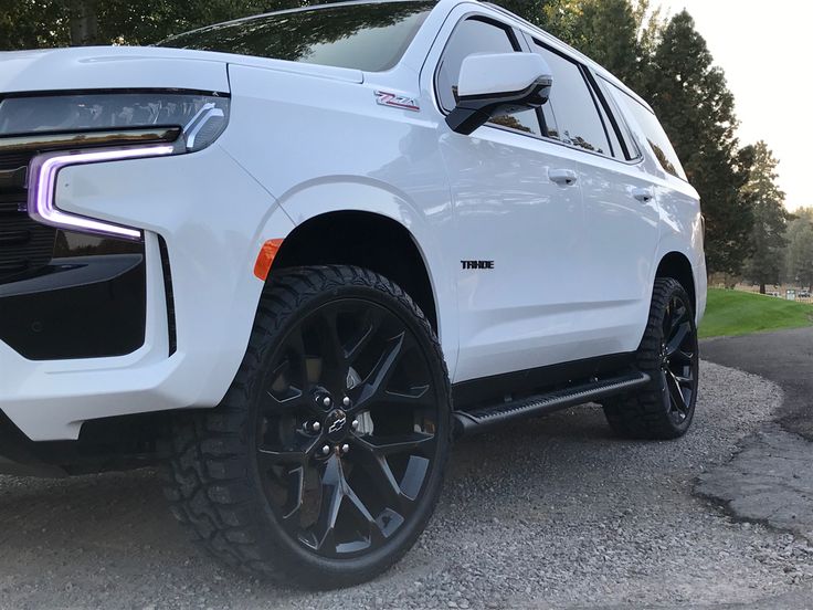 the front end of a white truck parked in a parking lot next to some trees