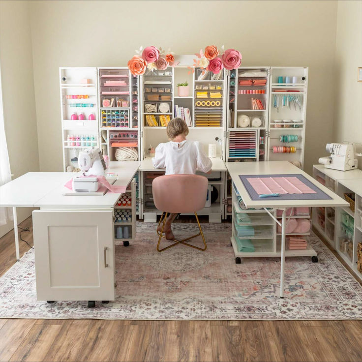 a woman sitting at a desk in front of a bookcase filled with craft supplies