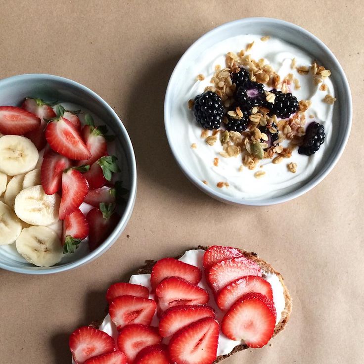 two bowls of yogurt, strawberries and granola sit next to each other