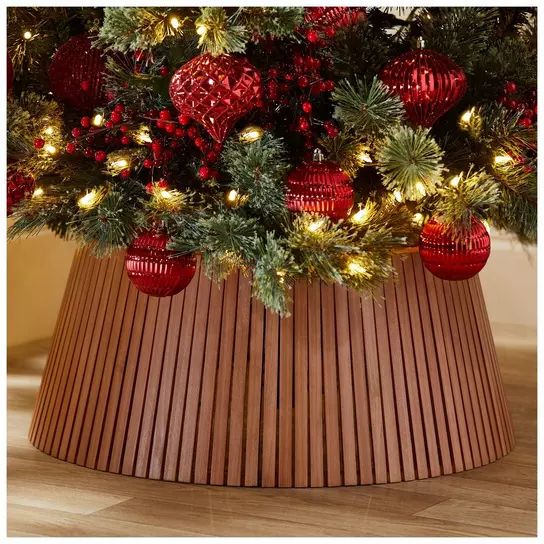 a christmas tree with red ornaments and lights in a wooden basket on the floor next to a wall