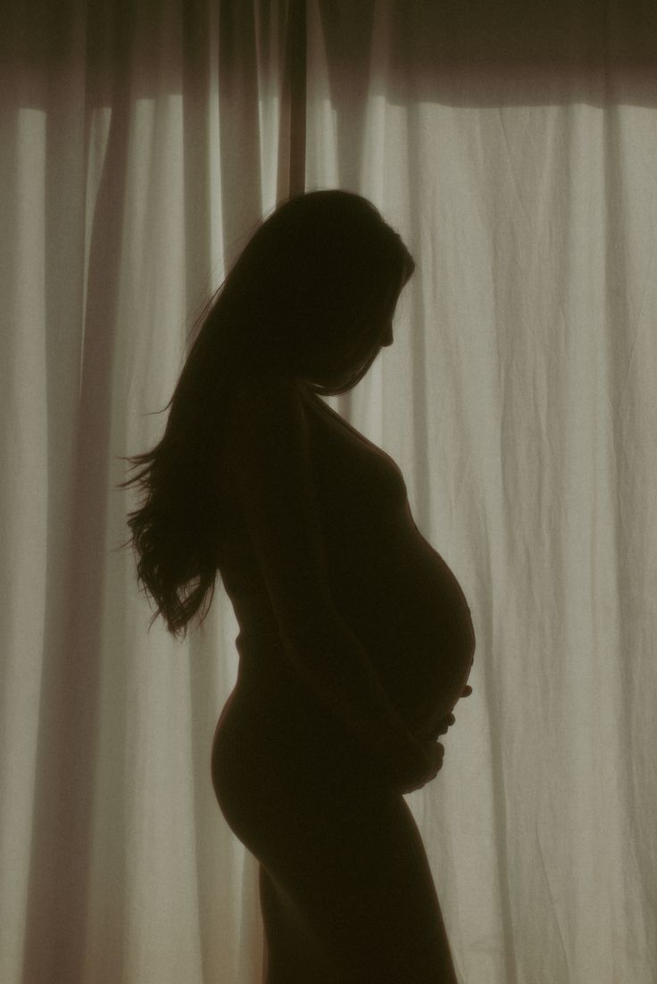 the silhouette of a pregnant woman in front of a curtain with her hands on her hips