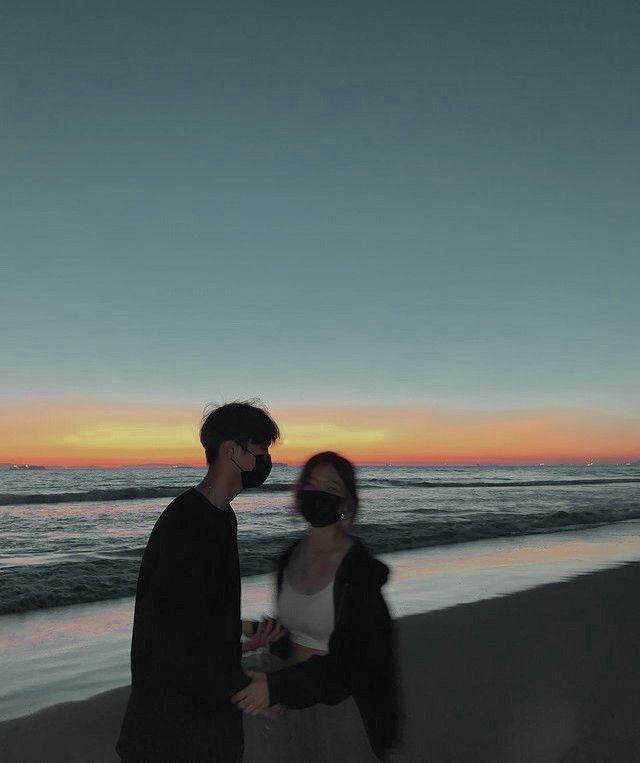 two people standing on the beach at sunset