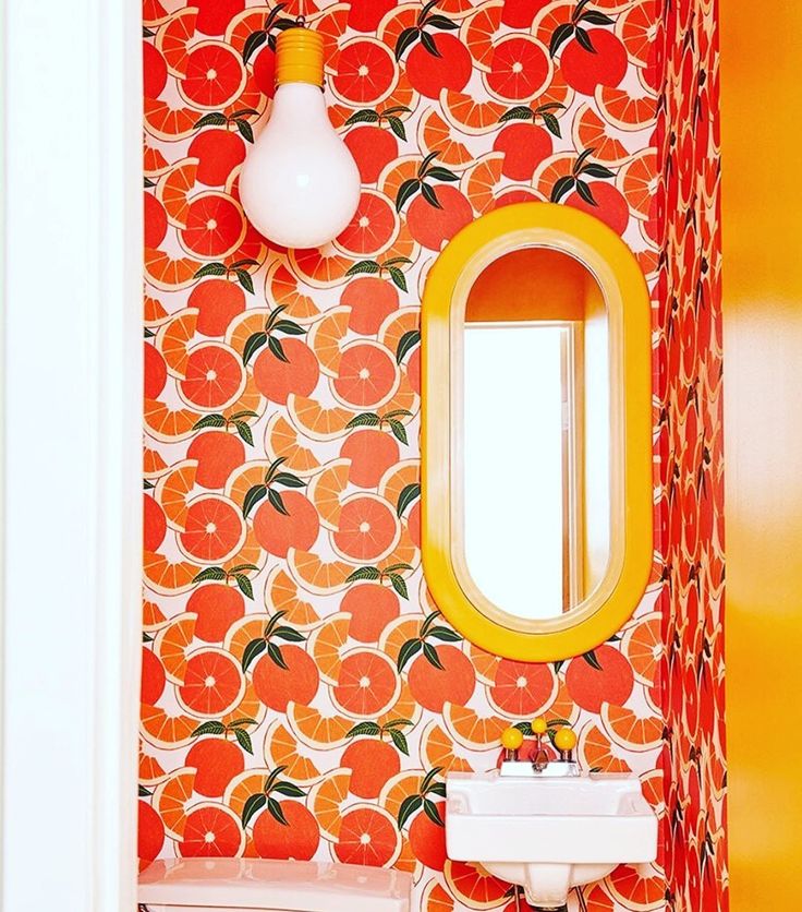 a bathroom with orange wallpaper and an oval mirror on the wall next to a sink