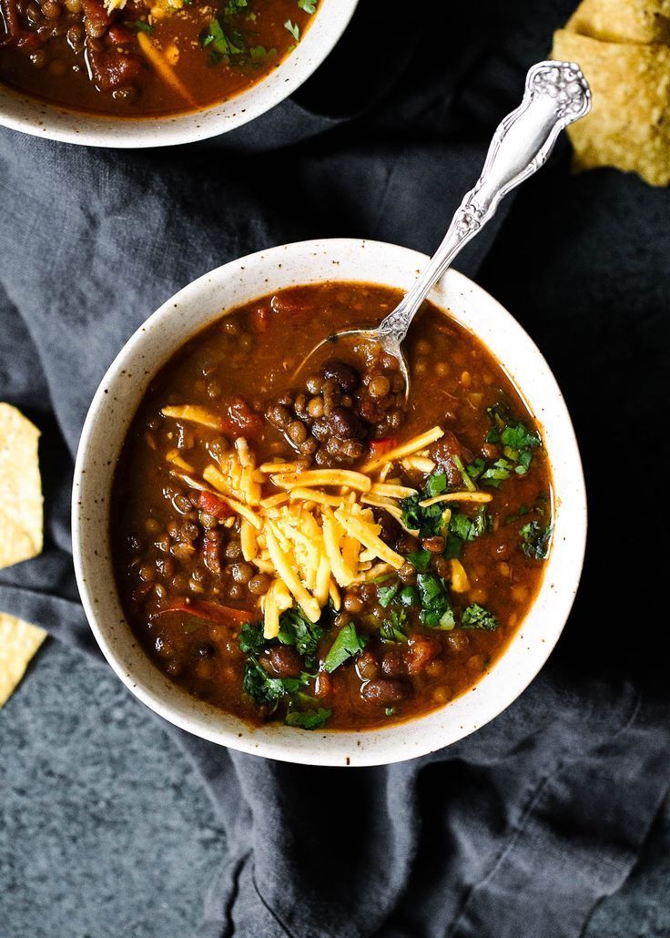 two bowls filled with chili and beans next to tortilla chips on a black cloth