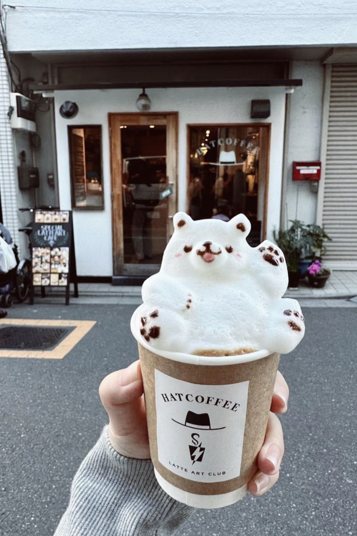 a person holding up a cup of ice cream in front of a building with a bear on it