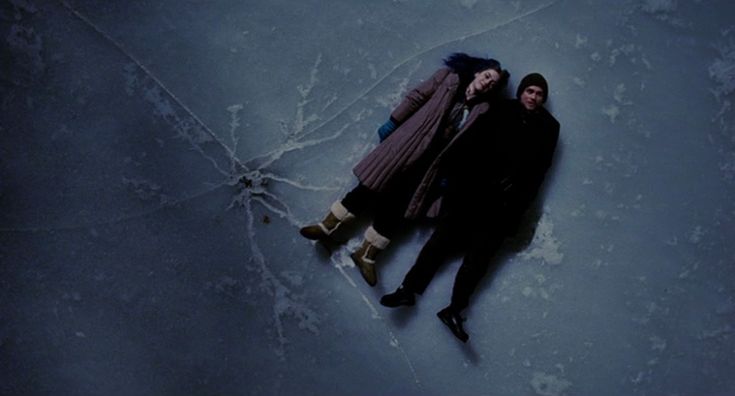 two people are laying on the snow with their arms around each other and one person is holding an umbrella