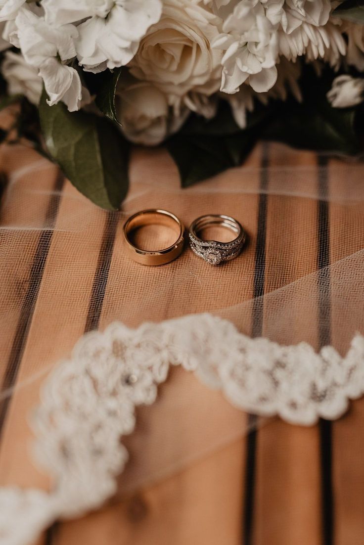 two wedding rings sitting on top of a wooden table next to white flowers and greenery