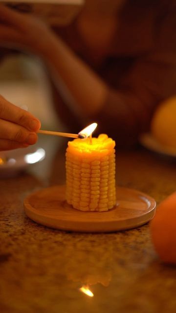 a person lighting a candle on top of a wooden plate with corn on the cob