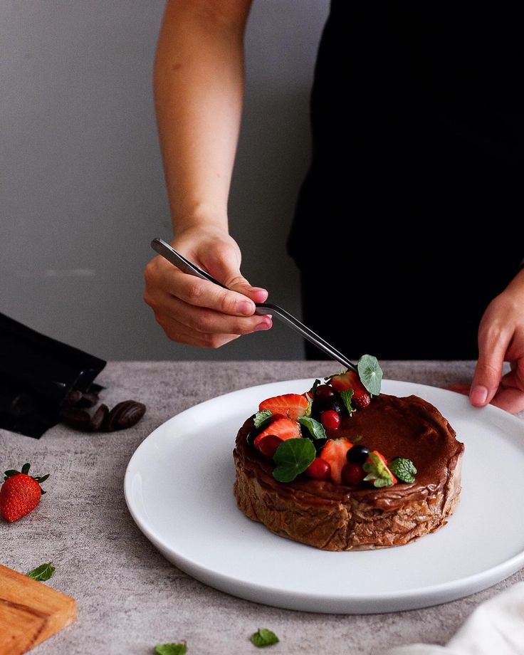 a person cutting into a chocolate cake with fruit on top