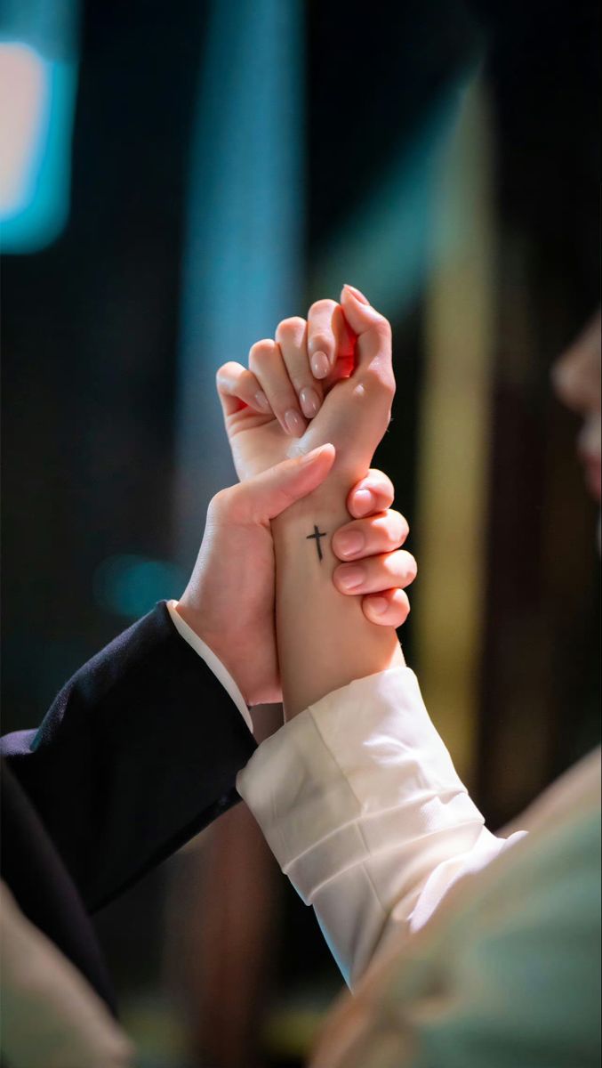 two people holding hands with a cross tattoo on their wrist and the other hand above them