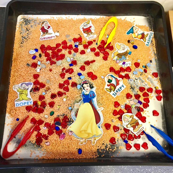 there are many stickers and scissors on the baking sheet that is covered in sand