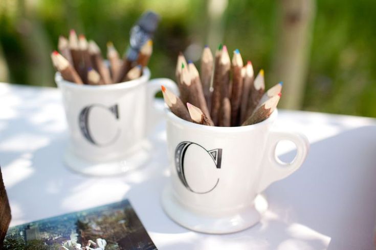 two mugs filled with pencils sitting on top of a table next to a book