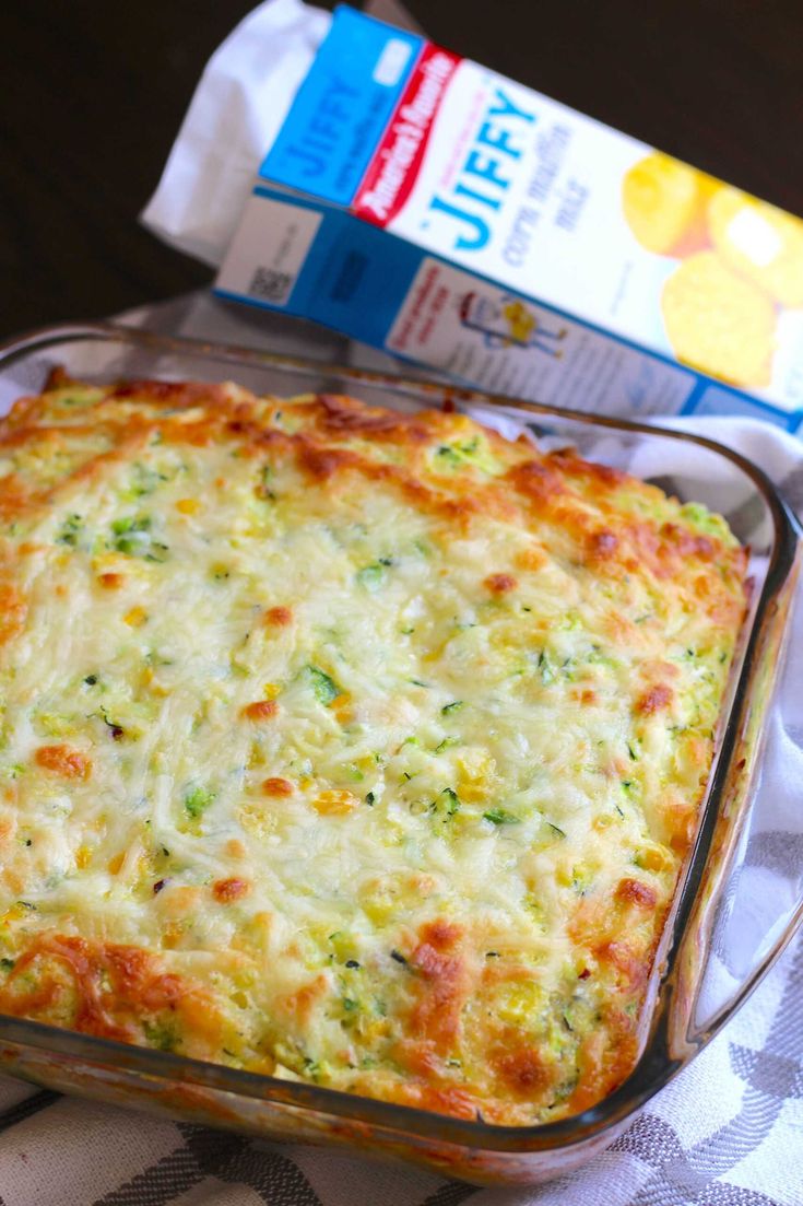 a casserole dish with cheese and broccoli in it next to a carton of juice