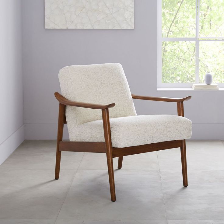 a white chair sitting in front of a window next to a painting on the wall