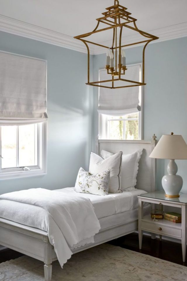 a bedroom with blue walls, white bedding and a chandelier hanging from the ceiling