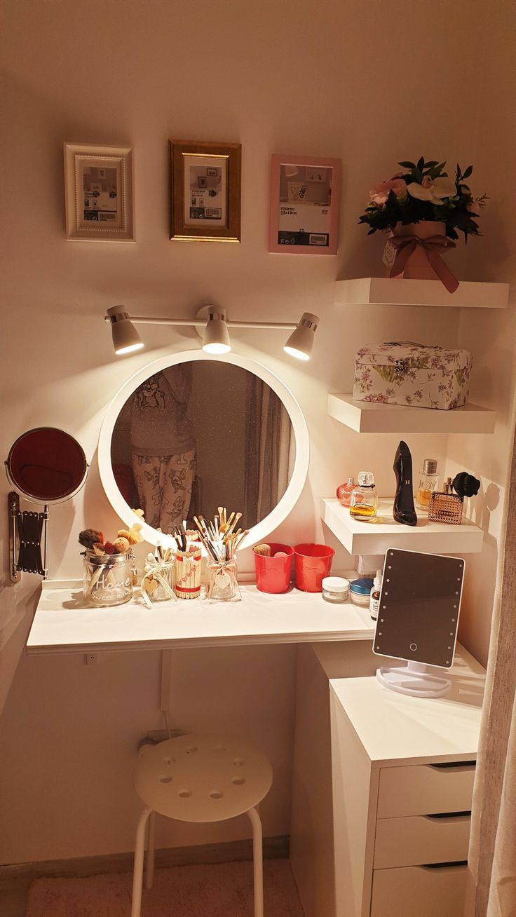 a white desk topped with a round mirror next to a stool and shelf filled with items