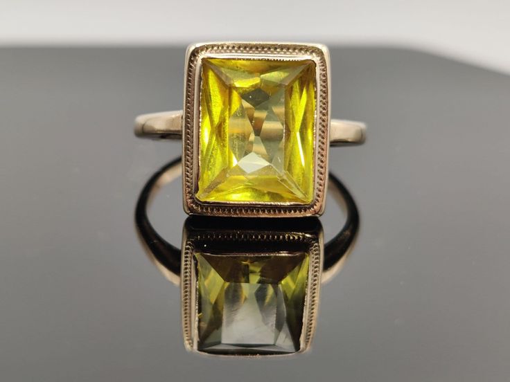 A uniquely faceted retro travel ring. It was made as a safe travel piece , while the real yellow saphirre or diamond ring set in 18k remained  under lock and key.  The rectagular stone has a fancy cut and is bezel set in gold with a fine gold braid wrapping the setting beautifully.  The travel pieces were usually set in 8 or 9kt in UK and 10k in the US. The shank on this ring shows no stamp.  Am pricing it as gold filled   Very Good Vintage Condition  please view photos carefully  approx. size 4 Yellow Rectangular Gemstone Rings, Classic Yellow Faceted Rings, Classic Yellow Rectangular Rings, Formal Yellow Rectangular Rings, Hallmarked Rectangular Emerald Ring, Yellow Rectangular Anniversary Ring, Vintage Yellow Rectangular Jewelry, Vintage Gold Rectangular Emerald Ring, Art Deco Gold Rings With Rectangular Stone