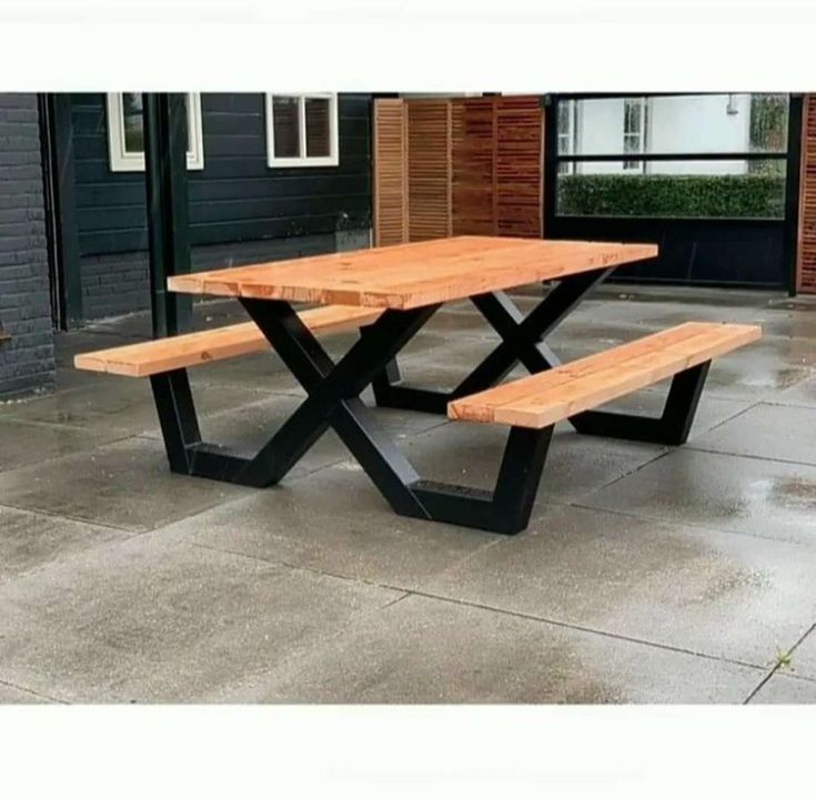 a wooden bench sitting on top of a cement floor next to a building with windows