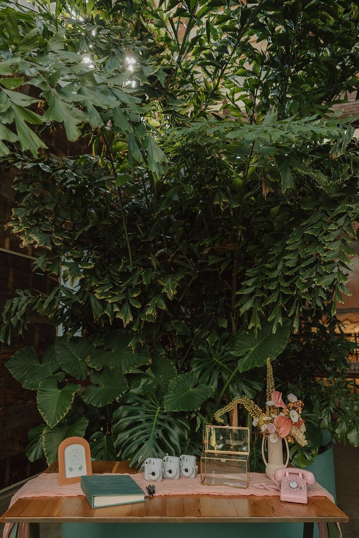 a wooden table topped with lots of green plants and candles next to a plant covered wall