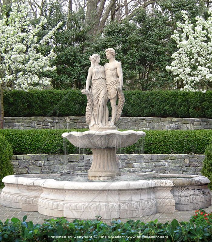 a fountain in the middle of a garden with two people standing on top of it