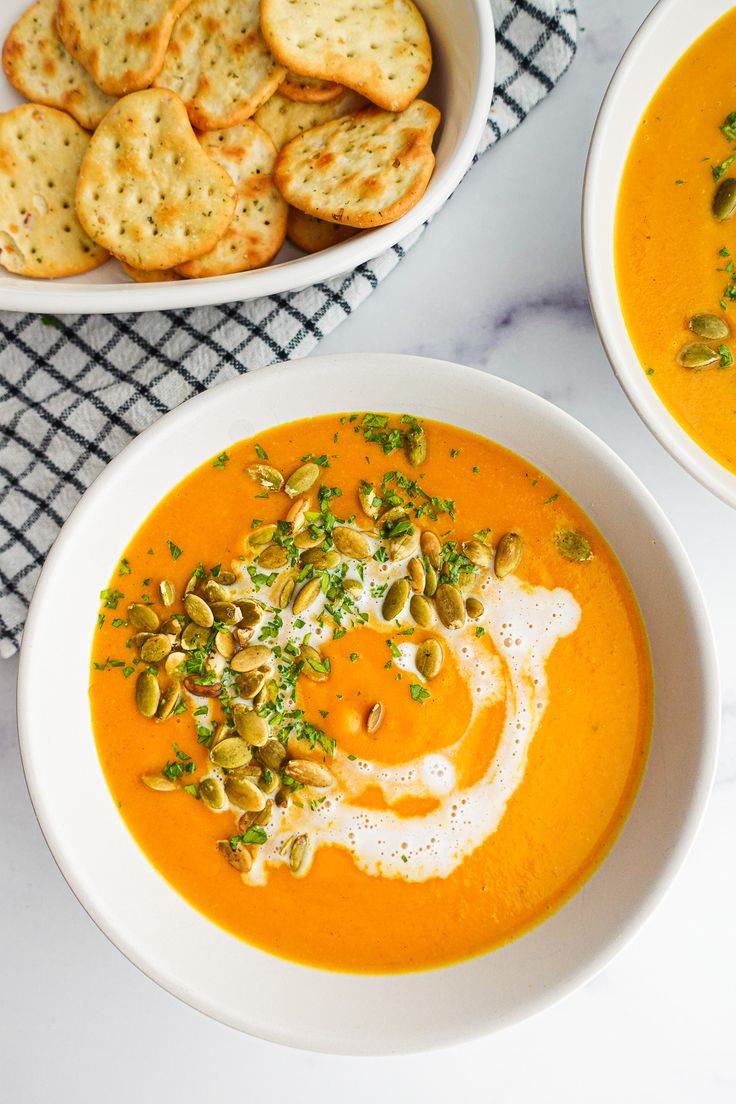 two bowls of carrot soup with crackers on the side