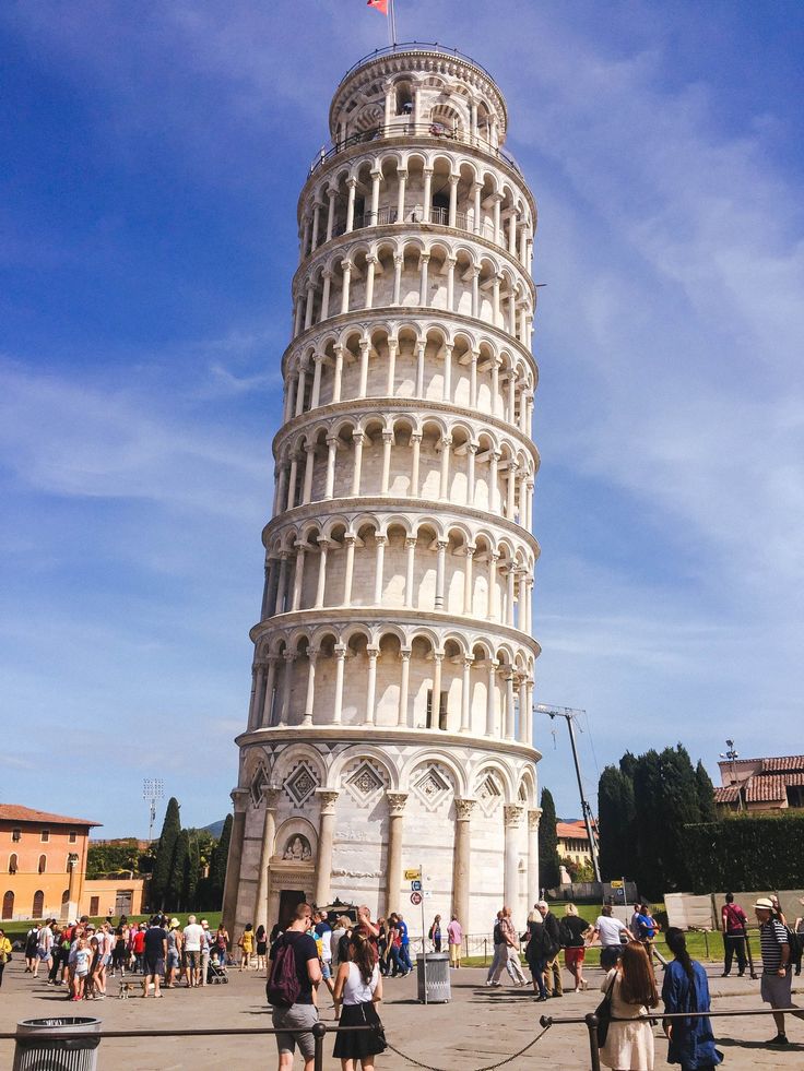 people standing in front of the leaning tower with blue sky behind it and clouds overhead