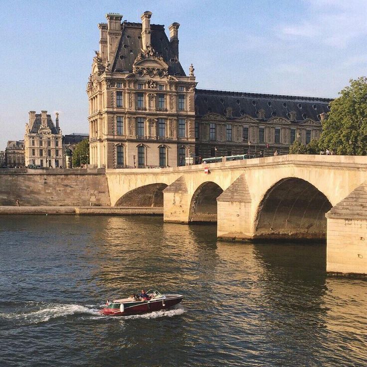 a small boat traveling down the river in front of a large stone bridge and old buildings