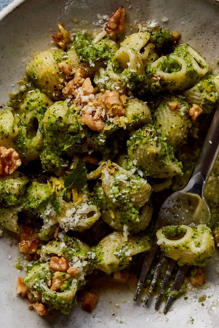 a white plate topped with broccoli covered in pesto and walnuts next to a fork